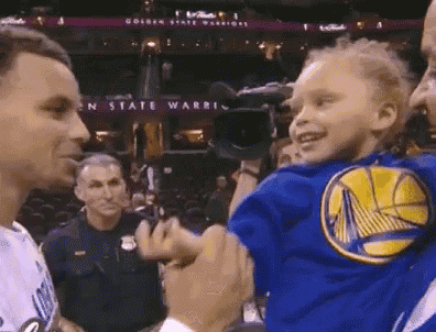 a young boy wearing a golden state warriors shirt is being held by a basketball player .