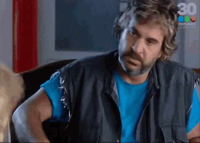 a man with a beard is wearing a blue shirt and a black leather vest .