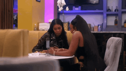 two women sit at a table in a restaurant looking at their phones