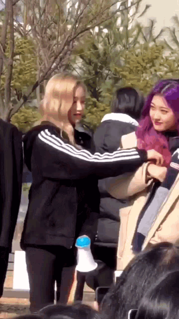 a woman with purple hair is standing next to another woman in a crowd .