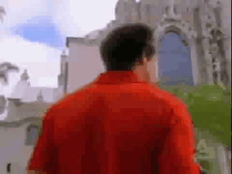 a man in a red shirt is walking in front of a building with a blue door .
