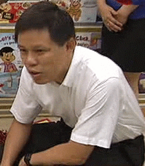 a man in a white shirt is kneeling down in front of a stack of books