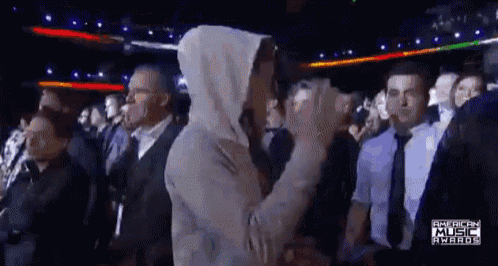 a man in a hooded sweatshirt is standing in a crowd at the american music awards .