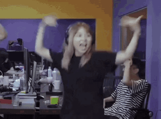 a woman wearing headphones is dancing in an office with her arms in the air