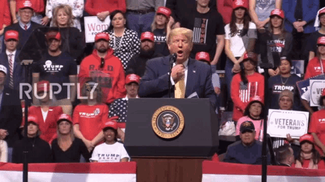 a man stands at a podium with a sign that says veterans for trump in front of him