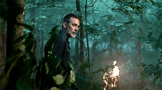a man with a beard is standing in a dark forest