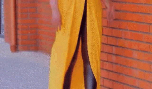 a woman in a yellow dress is standing in front of a brick wall