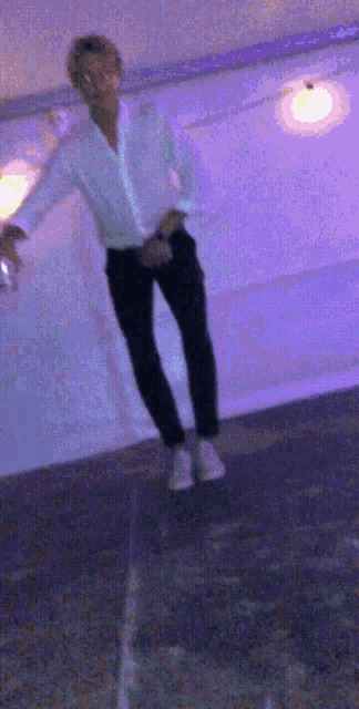 a man in a white shirt and black pants is standing in front of a purple wall