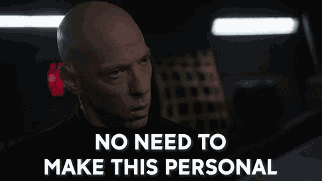 a bald man says " no need to make this personal " in a dark room