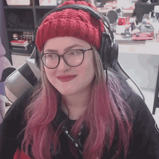 a woman with pink hair and glasses wearing a red hat