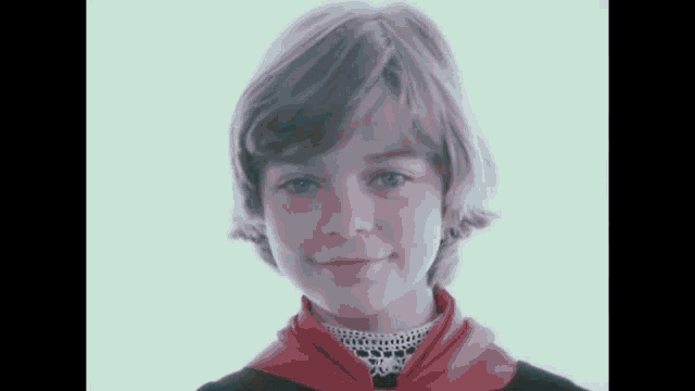 a young girl wearing a red scarf and a black shirt is smiling for the camera .