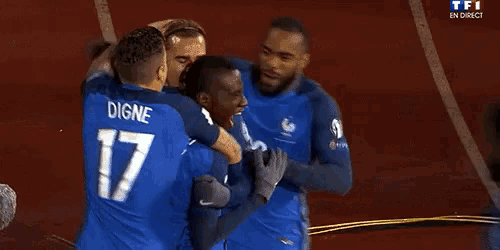 a group of soccer players are hugging each other on a field . one of the players has the number 17 on his shirt .