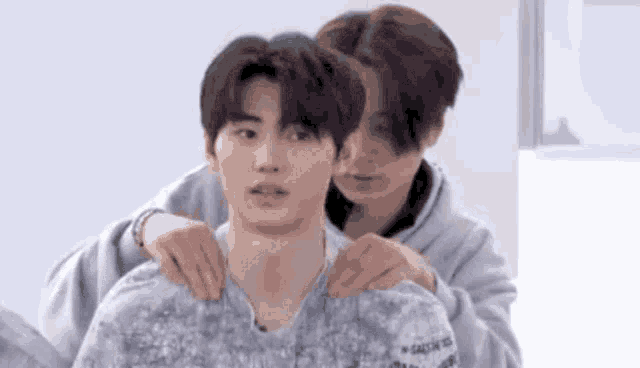 two young men are hugging each other in a room . one of the men is putting his arm around the other 's neck .