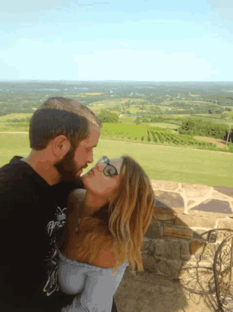a man and a woman are kissing with a view of a vineyard in the background