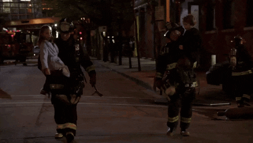two firefighters are carrying a child down a street in front of a building that says institute