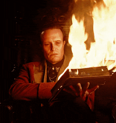a man in a red jacket holds a book that is on fire
