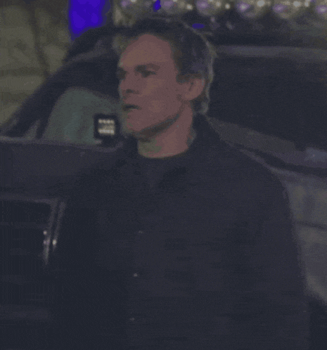a man in a black jacket is standing in front of a vehicle