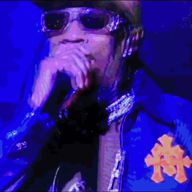 a man wearing sunglasses is singing into a microphone in a blue jacket