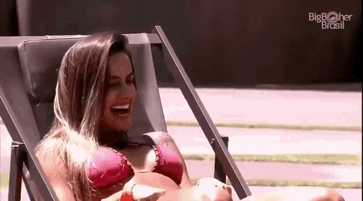 a woman in a bikini is sitting in a beach chair and laughing