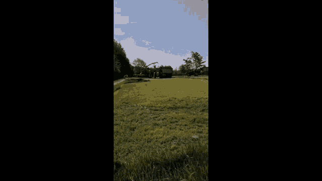 a tractor is cutting grass in a field with a crane and a truck .