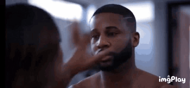 a shirtless man with a beard is looking at himself in the mirror .