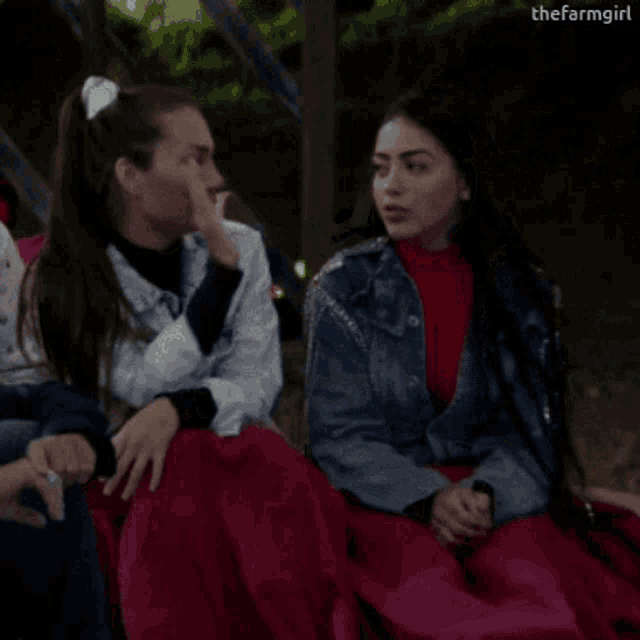 a group of women are sitting on a bench and one of them is wearing a denim jacket .