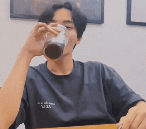 a man wearing a t-shirt that says vida is drinking from a glass while sitting at a table .
