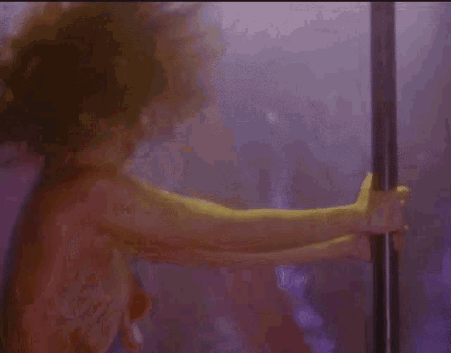 a naked woman is standing next to a pole in a purple room .