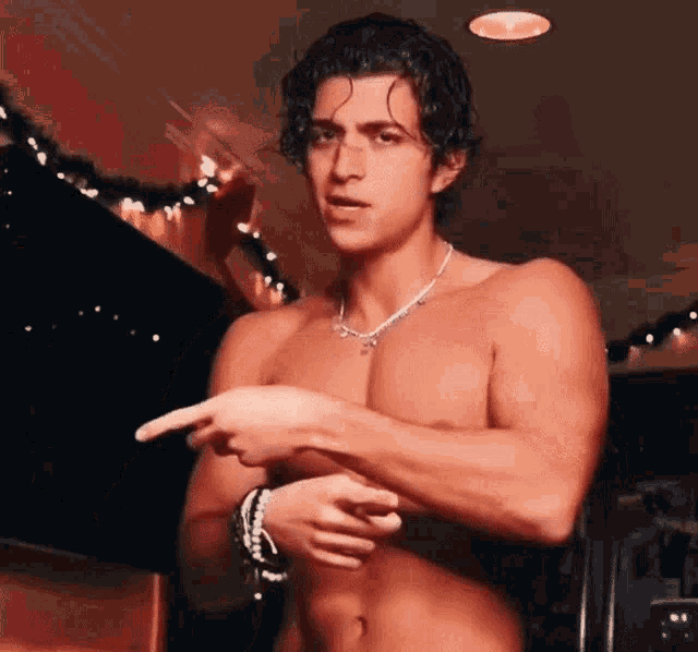 a shirtless man wearing a necklace is pointing to his chest .