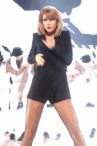 a woman in a black jumpsuit is dancing in front of a group of men