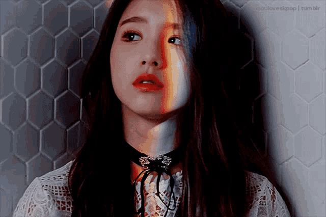 a woman with a choker around her neck is standing in front of a wall with a honeycomb pattern