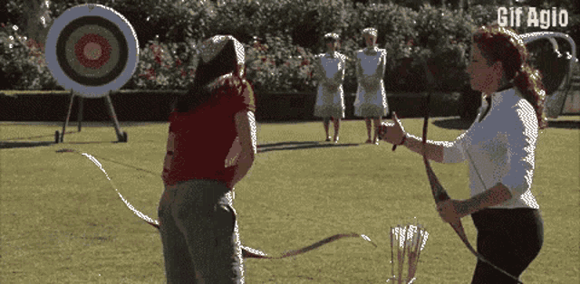 a woman is holding a bow and arrow in front of a target that says gif agio on the bottom