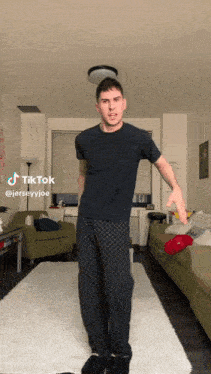 a man in a black shirt and grey pants is standing in a living room with a tiktok sticker on the bottom