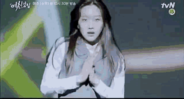 a girl is standing on a stage with her hands folded in front of her face .