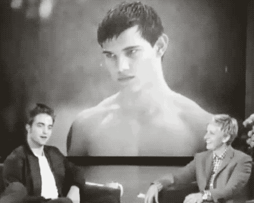 two men are sitting in front of a screen with a picture of a shirtless man on it .