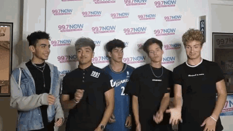 a group of young men stand in front of a wall that says 997 now