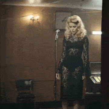 a woman in a black lace dress is standing in front of a microphone