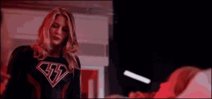 a woman in a black superhero costume is standing next to a woman in a bed .