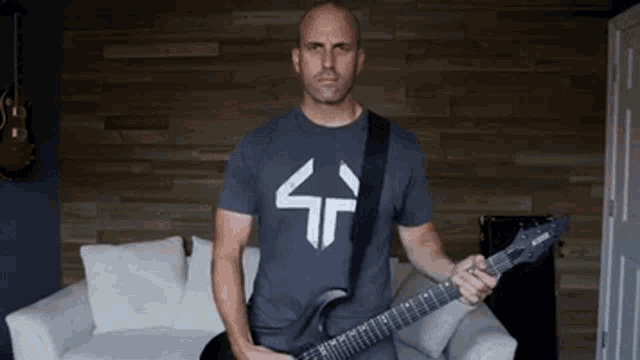 a man in a gray shirt is holding a guitar in front of a wooden wall .