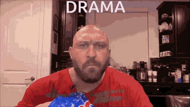 a bald man with a beard is holding a bag of popcorn in front of a sign that says ' drama '
