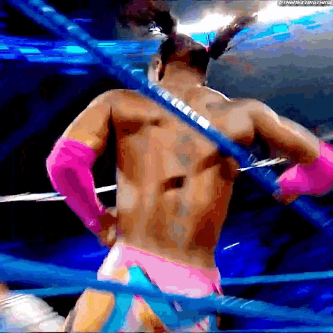 a wrestler in a pink and blue outfit is standing in a ring .