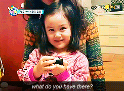 a little girl is holding a camera while being held by a woman and asking what do you have there