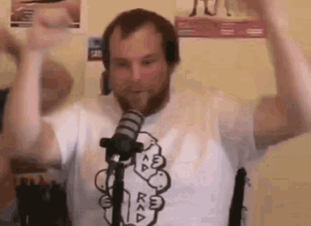 a man with a beard is standing in front of a microphone with his hands in the air