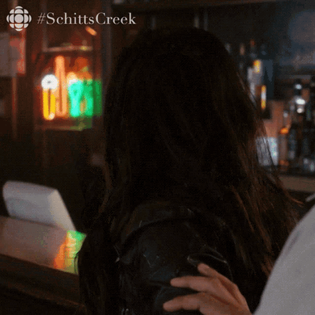 a woman sitting at a bar with #schitts creek written on the bottom right