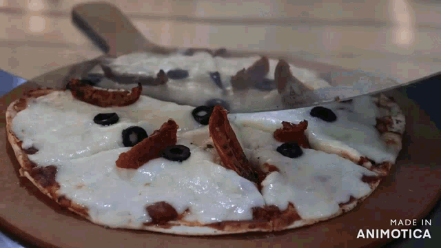 a pizza is being sliced on a wooden cutting board with the words made in animatica on the bottom right