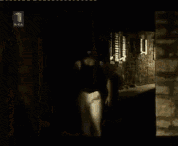 a woman in a black tank top is standing in a dark room in front of a television screen .