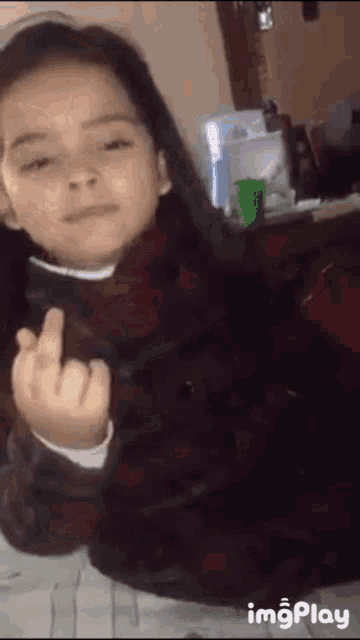 a little girl is giving the middle finger while wearing a plaid shirt .