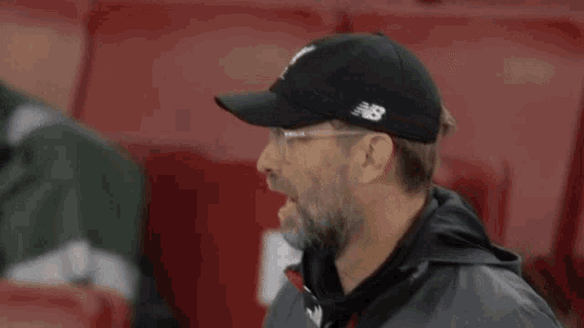 a man wearing glasses and a hat is sitting in a stadium .