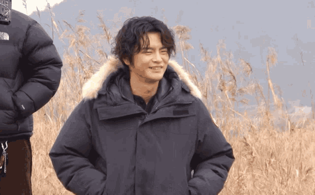 a man wearing a black north face jacket stands in a field of tall grass