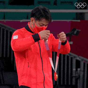 a man wearing a red jacket and a mask is holding a medal